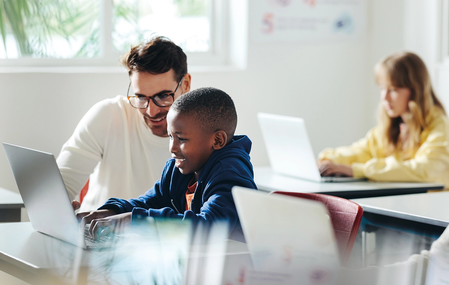 Teacher helping a student on a laptop in class.